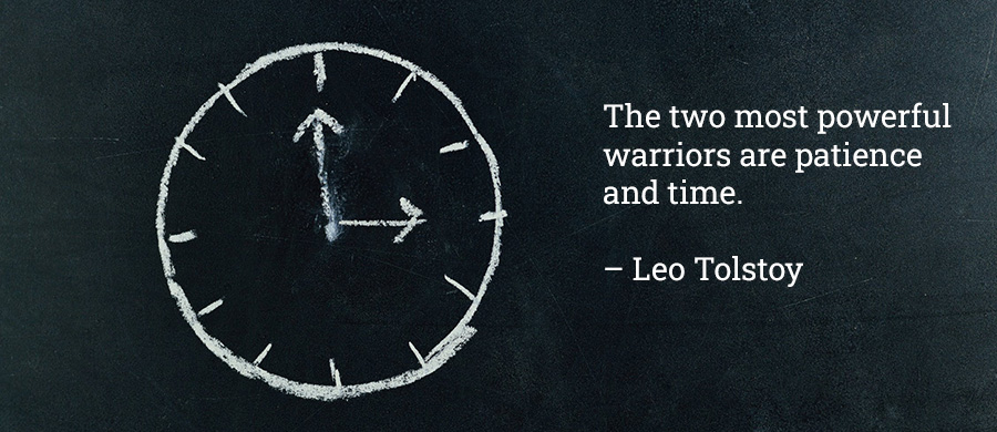 Clock on blackboard with quote by Leo Tolstoy saying "The two most powerful warriors are patience and time."